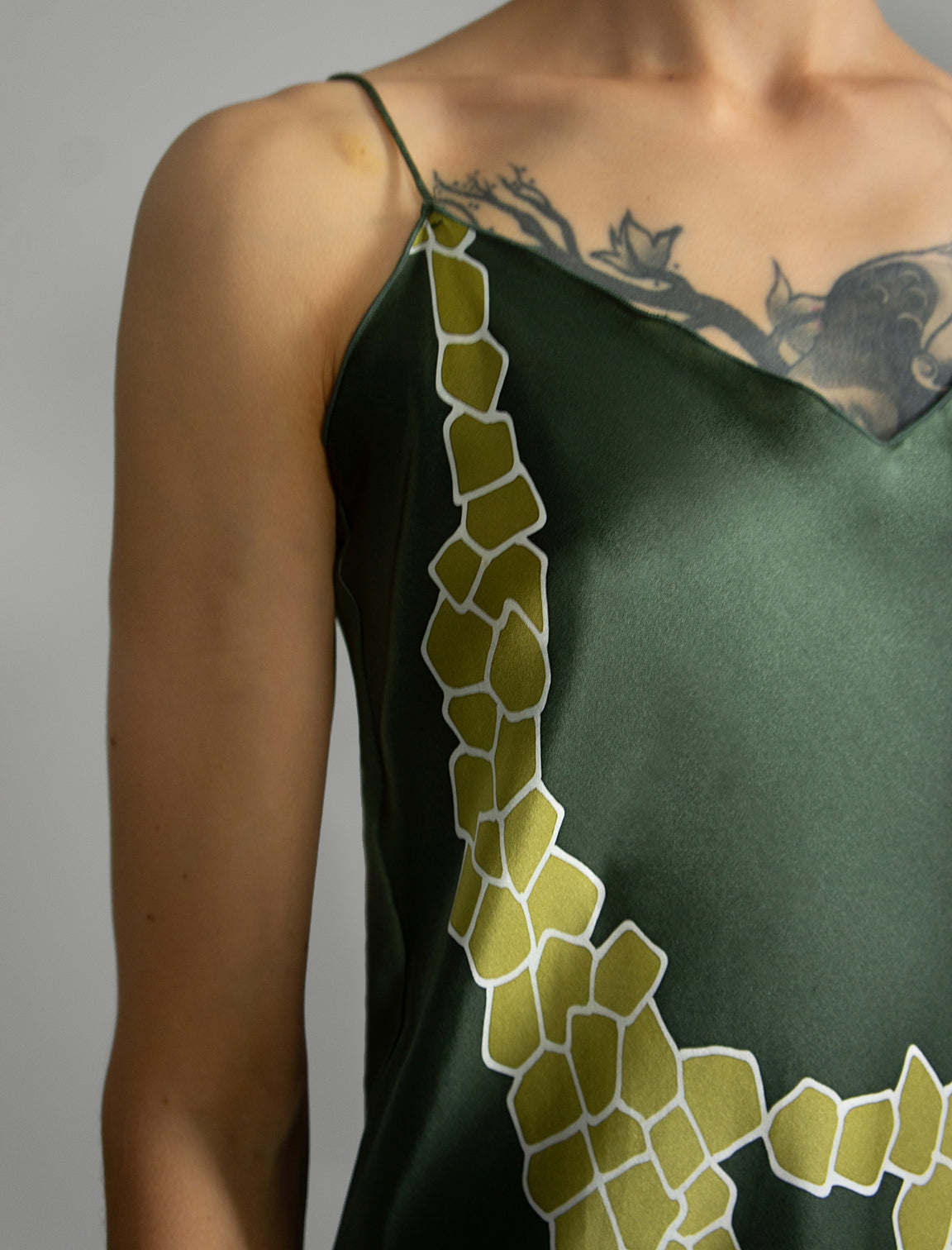 Strap and neckline detail: Elegant long body contouring silk dress in forest green colour with contrasting green graphic Macrosnake batik motif, featuring spaghetti straps, V-neckline and a fluid contemporary silhouette.