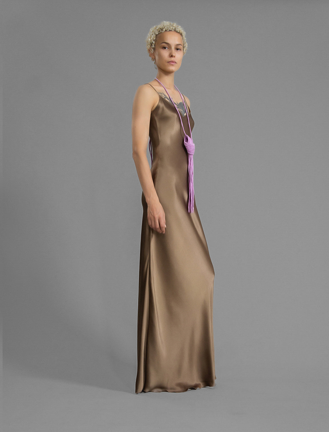 Side view. Elegant long body contouring silk dress in soft mocha colour, featuring spaghetti straps, V-neckline and a fluid contemporary silhouette.