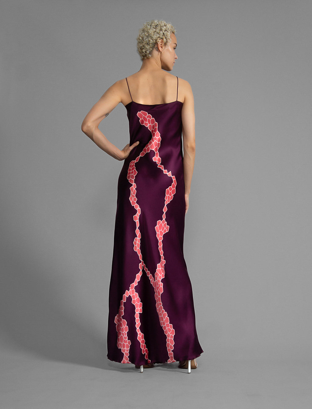 Back View. Elegant long body contouring silk dress in deep vino colour with contrasting pink graphic Macrosnake batik motif, featuring spaghetti straps, V-neckline and a fluid contemporary silhouette.