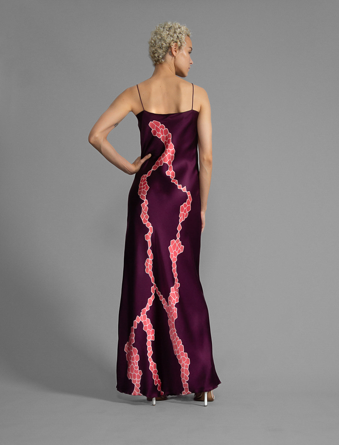 Back View. Elegant long body contouring silk dress in deep vino colour with contrasting pink graphic Macrosnake batik motif, featuring spaghetti straps, V-neckline and a fluid contemporary silhouette.
