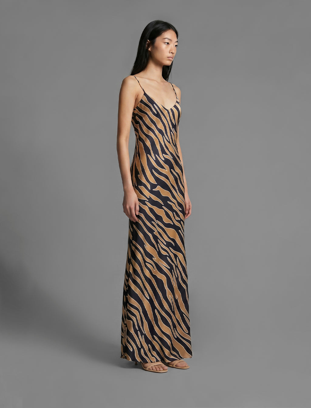 Side view. Elegant long body contouring silk dress in black colour with contrasting tobacco graphic Zebra batik motif, featuring spaghetti straps, V-neckline and a fluid contemporary silhouette.