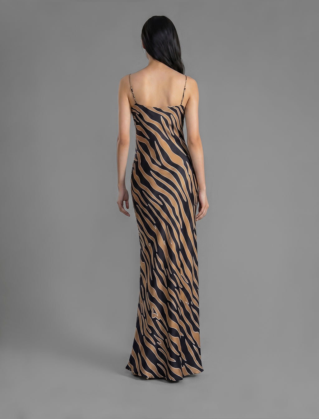 Back view. Elegant long body contouring silk dress in black colour with contrasting tobacco graphic Zebra batik motif, featuring spaghetti straps, V-neckline and a fluid contemporary silhouette.