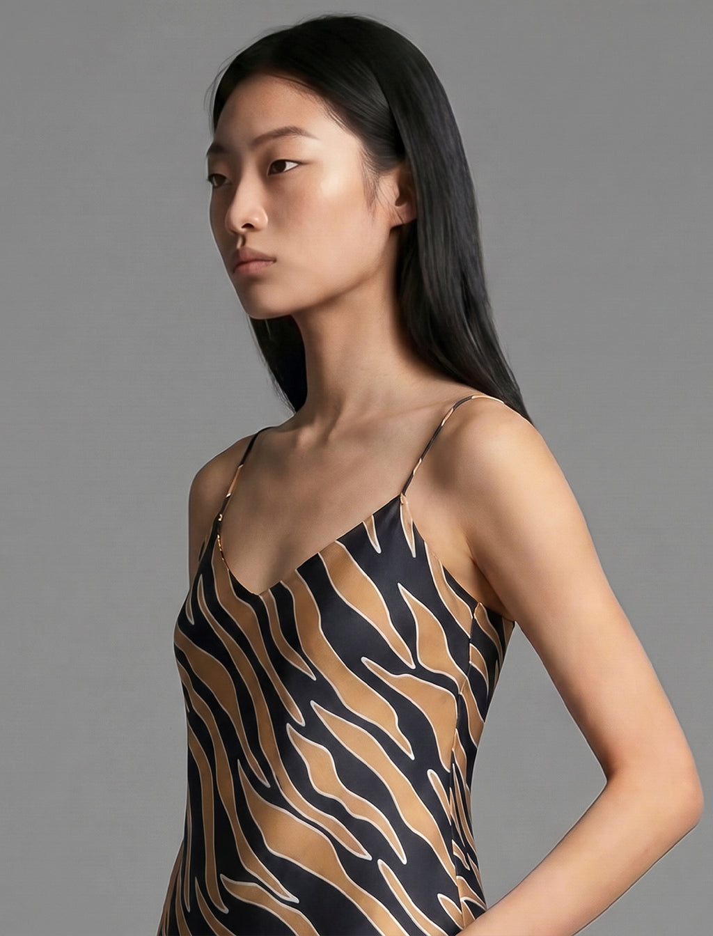 Neckline detail. Elegant long body contouring silk dress in black colour with contrasting tobacco graphic Zebra batik motif, featuring spaghetti straps, V-neckline and a fluid contemporary silhouette.