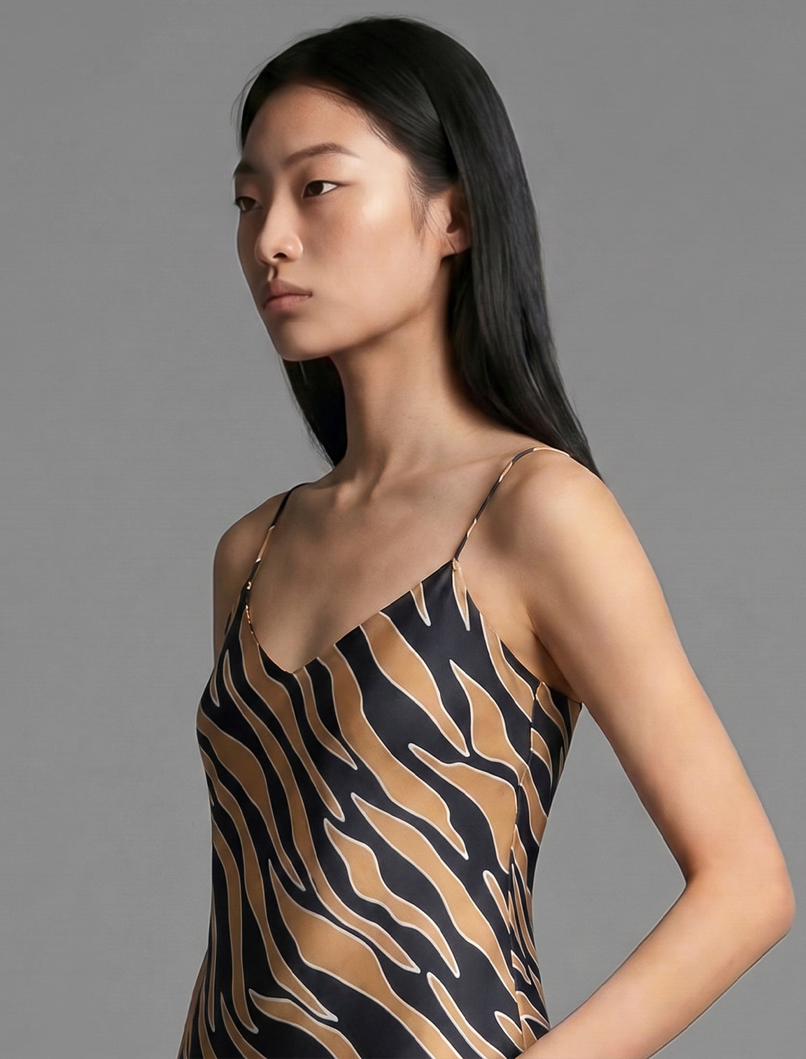 Neckline detail. Elegant long body contouring silk dress in black colour with contrasting tobacco graphic Zebra batik motif, featuring spaghetti straps, V-neckline and a fluid contemporary silhouette.