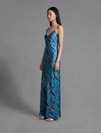 Side view. Elegant long body contouring silk dress in blue colour with contrasting deep blue graphic Zebra batik motif, featuring spaghetti straps, V-neckline and a fluid contemporary silhouette.