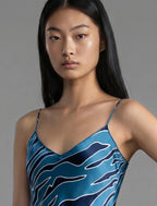 Neckline detail. Elegant long body contouring silk dress in blue colour with contrasting deep blue graphic Zebra batik motif, featuring spaghetti straps, V-neckline and a fluid contemporary silhouette.