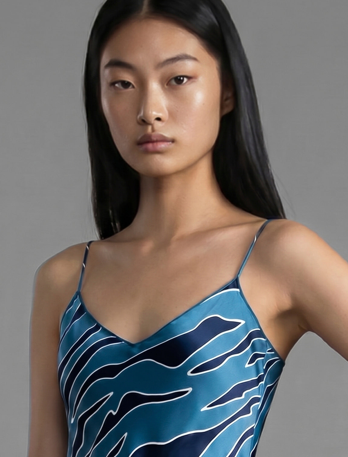 Neckline detail. Elegant long body contouring silk dress in blue colour with contrasting deep blue graphic Zebra batik motif, featuring spaghetti straps, V-neckline and a fluid contemporary silhouette.