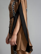 Sleeve detail: Elegant silk draped dress with graphic Macrosnake batik motif in black on warm tobacco colour, featuring fluid kimono sleeves, asymmetrical hemline, and relaxed contemporary silhouette with waist tie detail.