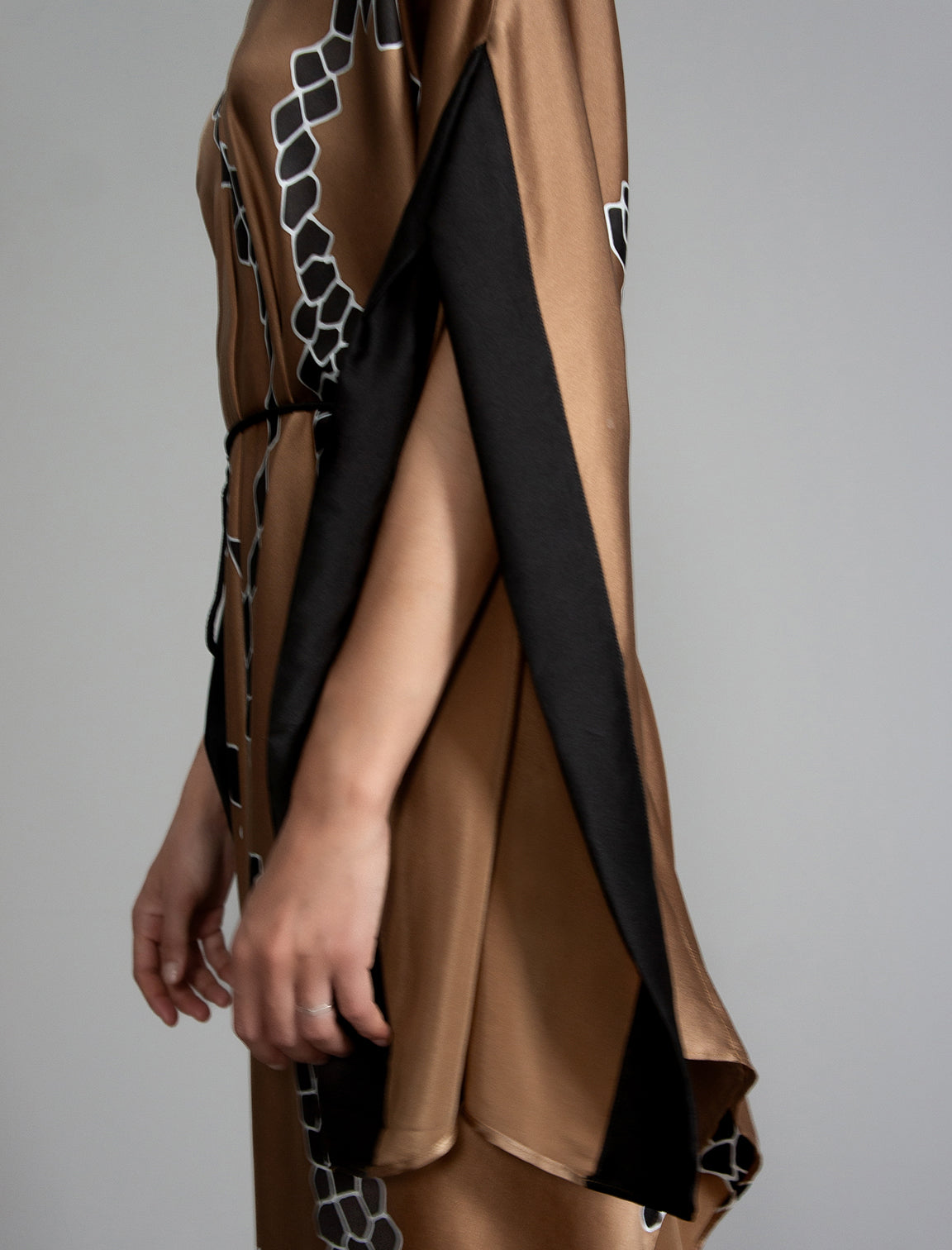 Sleeve detail: Elegant silk draped dress with graphic Macrosnake batik motif in black on warm tobacco colour, featuring fluid kimono sleeves, asymmetrical hemline, and relaxed contemporary silhouette with waist tie detail.