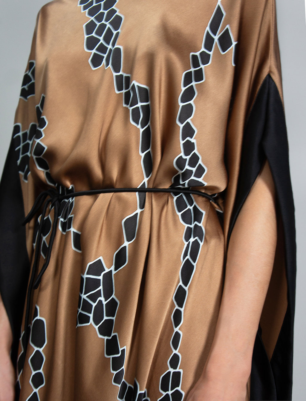 Waist detail: Elegant silk draped dress with graphic Macrosnake batik motif in black on warm tobacco colour, featuring fluid kimono sleeves, asymmetrical hemline, and relaxed contemporary silhouette with waist tie detail.