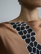 Neck detail: Elegant silk draped dress with graphic Macrosnake batik motif in black on warm tobacco colour, featuring fluid kimono sleeves, asymmetrical hemline, and relaxed contemporary silhouette with waist tie detail.
