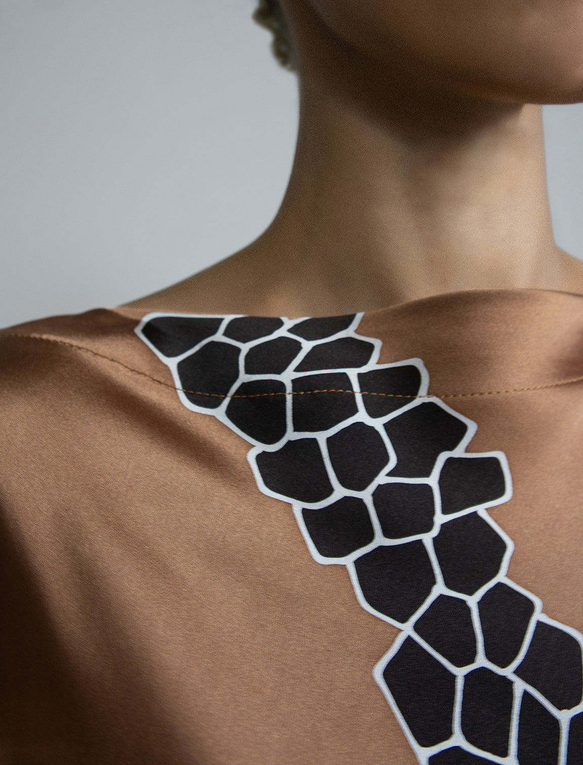 Neck detail: Elegant silk draped dress with graphic Macrosnake batik motif in black on warm tobacco colour, featuring fluid kimono sleeves, asymmetrical hemline, and relaxed contemporary silhouette with waist tie detail.