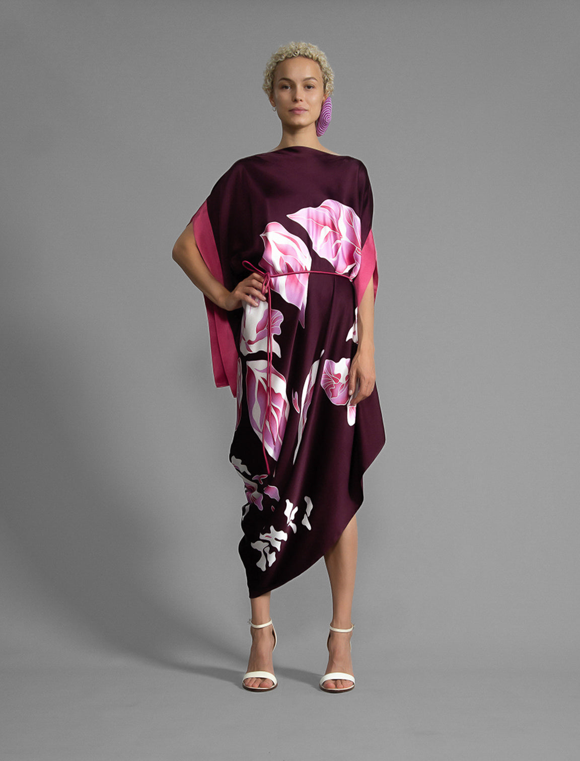 Front view 2. Elegant silk kaftan dress with oversized pink floral batik motif on deep vino colour silk, featuring flowing kimono sleeves, asymmetrical hemline, and relaxed contemporary silhouette.