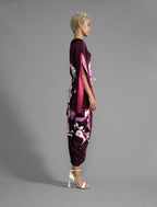 Side view. Elegant silk kaftan dress with oversized pink floral batik motif on deep vino colour silk, featuring flowing kimono sleeves, asymmetrical hemline, and relaxed contemporary silhouette.