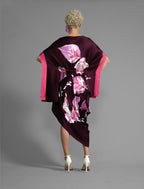 Back view. Elegant silk kaftan dress with oversized pink floral batik motif on deep vino colour silk, featuring flowing kimono sleeves, asymmetrical hemline, and relaxed contemporary silhouette.