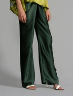 Close front view. Long silk pants in black forest green colour, featuring a knot tie at the front and a slick relaxed silhouette. 