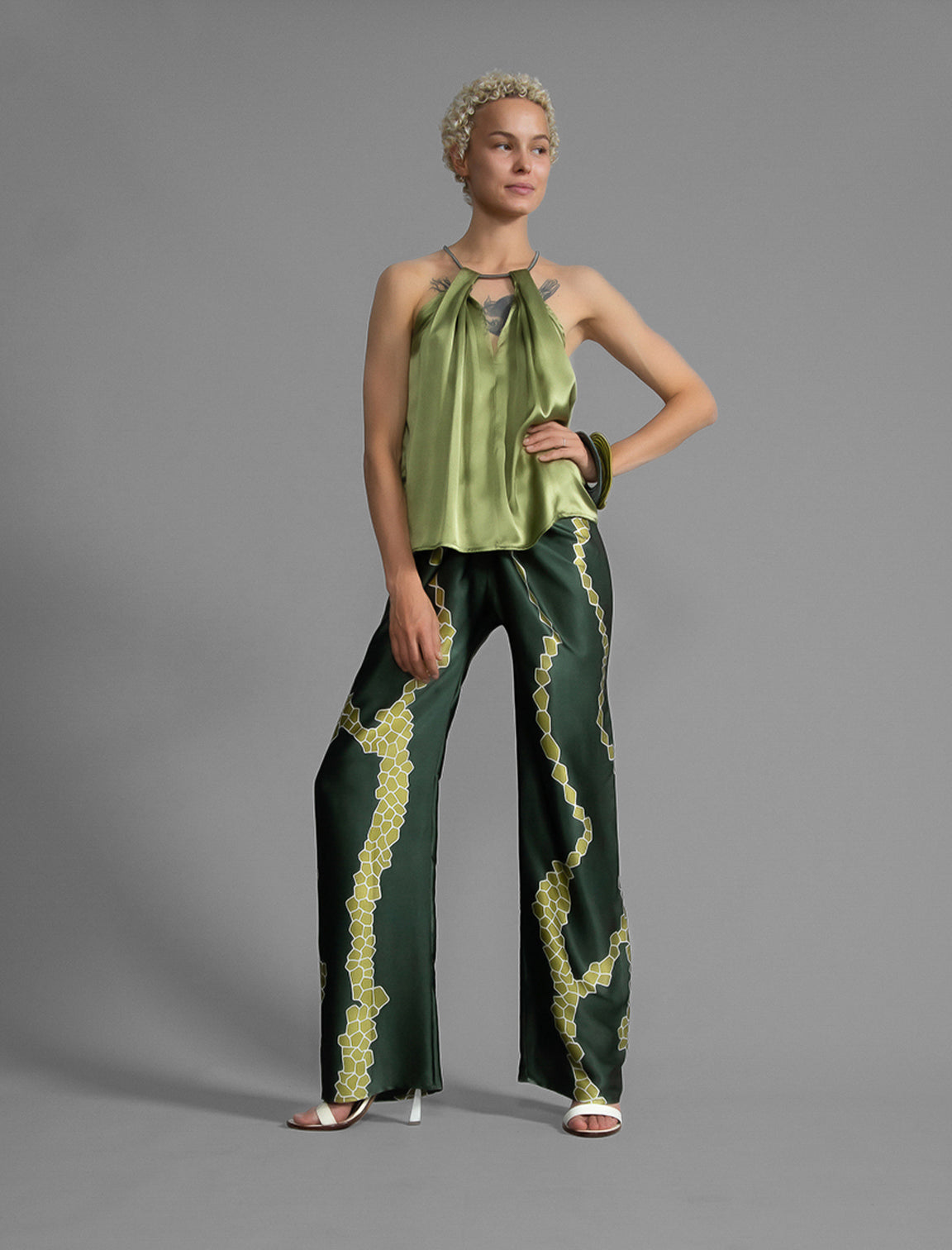 Front view. Long silk pants in forest green colour with contrasting blue graphic Macrosnake batik motif, featuring a knot tie at the front and a slick relaxed silhouette. 
