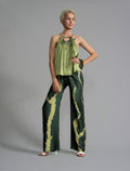 Front view. Long silk pants in forest green colour with contrasting blue graphic Macrosnake batik motif, featuring a knot tie at the front and a slick relaxed silhouette. 
