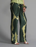 Close front view. Long silk pants in forest green colour with contrasting green graphic Macrosnake batik motif, featuring a knot tie at the front and a slick relaxed silhouette. 