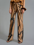 Close front view. Long silk pants in tobacco colour with contrasting blue graphic Macrosnake batik motif, featuring a knot tie at the front and a slick relaxed silhouette. 