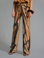 Close front view. Long silk pants in tobacco colour with contrasting blue graphic Macrosnake batik motif, featuring a knot tie at the front and a slick relaxed silhouette. 