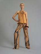 Front view. Long silk pants in tobacco colour with contrasting blue graphic Macrosnake batik motif, featuring a knot tie at the front and a slick relaxed silhouette. 