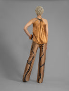 Back view. Long silk pants in tobacco colour with contrasting blue graphic Macrosnake batik motif, featuring a knot tie at the front and a slick relaxed silhouette. 