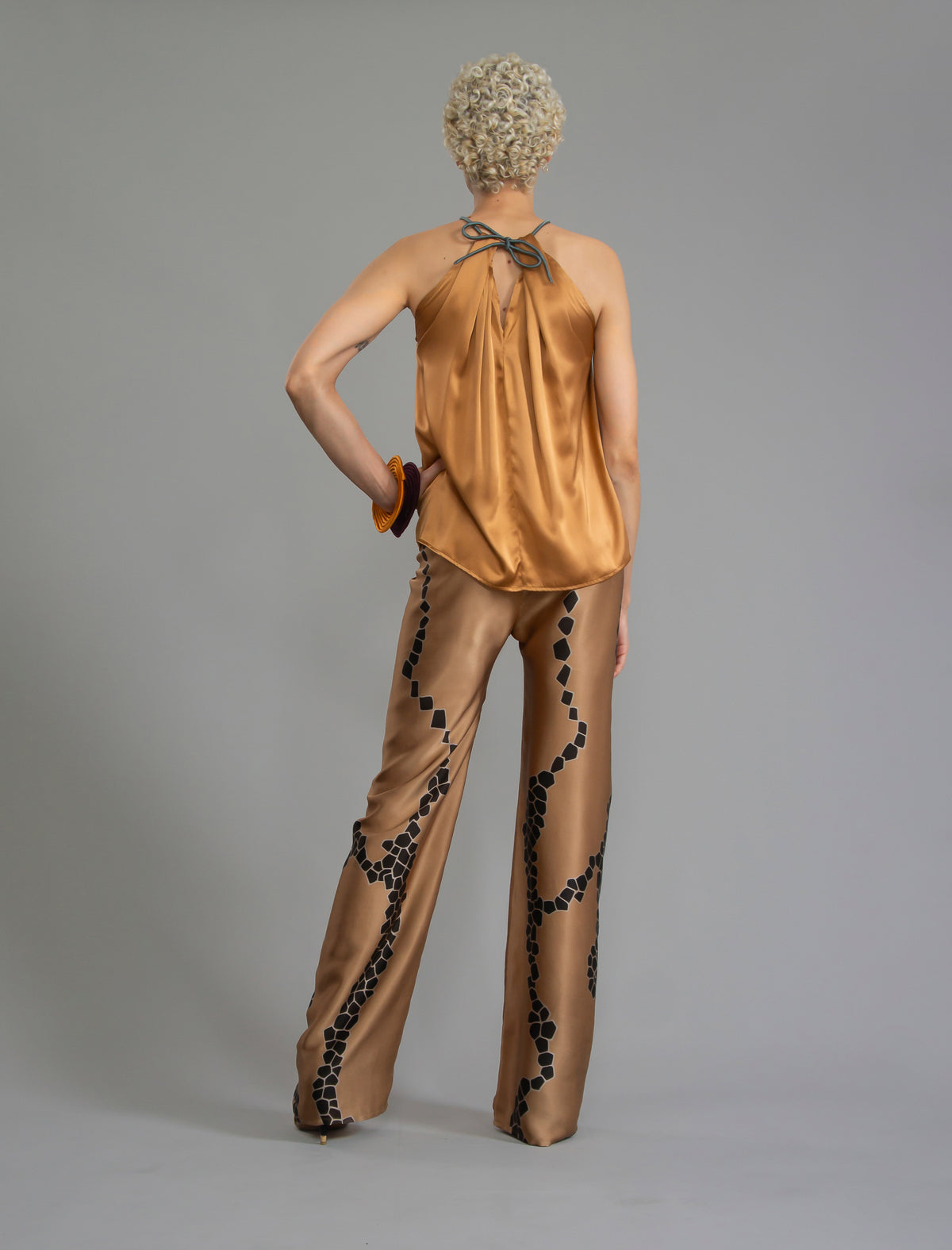 Back view. Long silk pants in tobacco colour with contrasting blue graphic Macrosnake batik motif, featuring a knot tie at the front and a slick relaxed silhouette. 