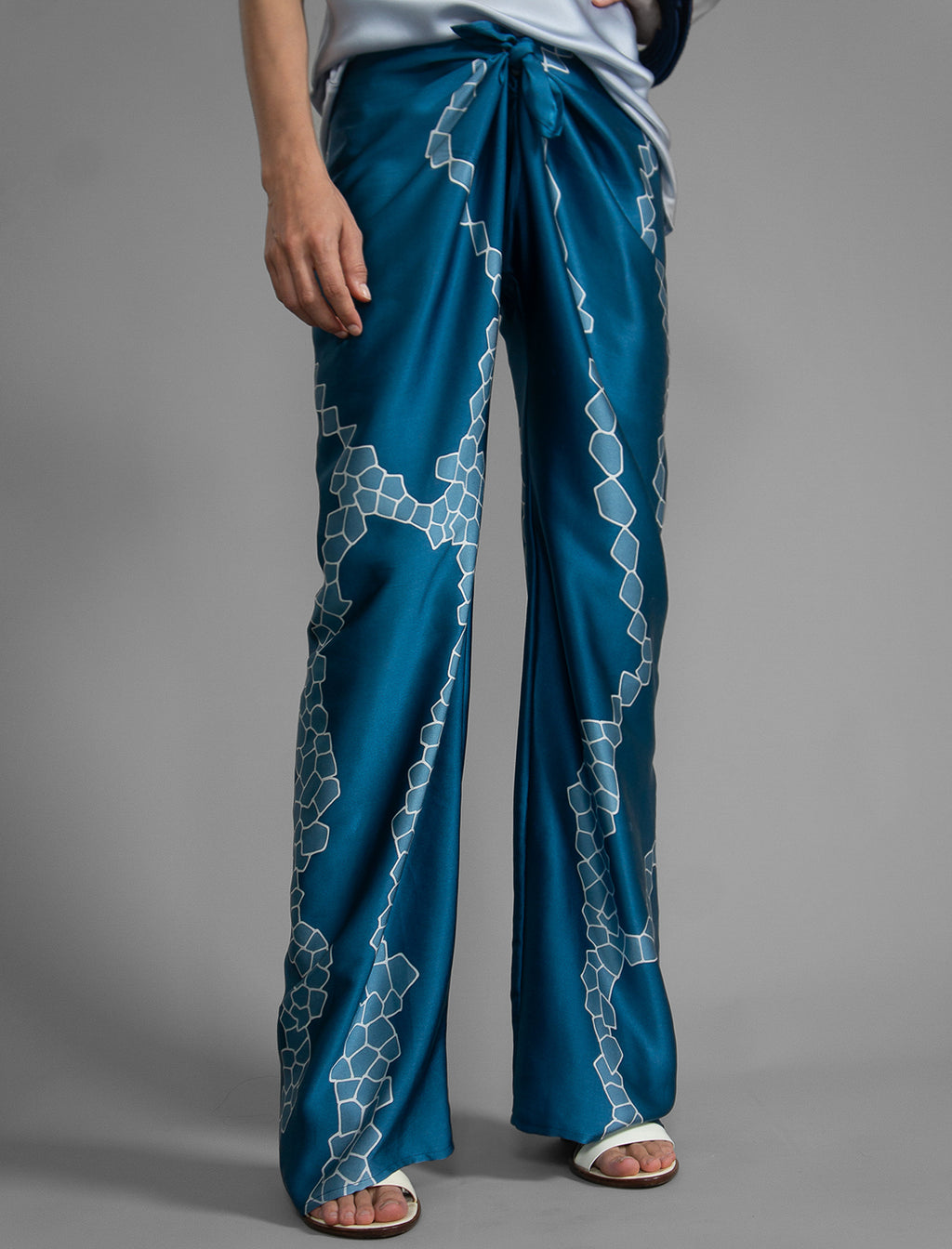 Close front view. Long silk pants in saxony blue colour with contrasting blue graphic Macrosnake batik motif, featuring a knot tie at the front and a slick relaxed silhouette. 