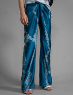 Close front view. Long silk pants in saxony blue colour with contrasting blue graphic Macrosnake batik motif, featuring a knot tie at the front and a slick relaxed silhouette. 