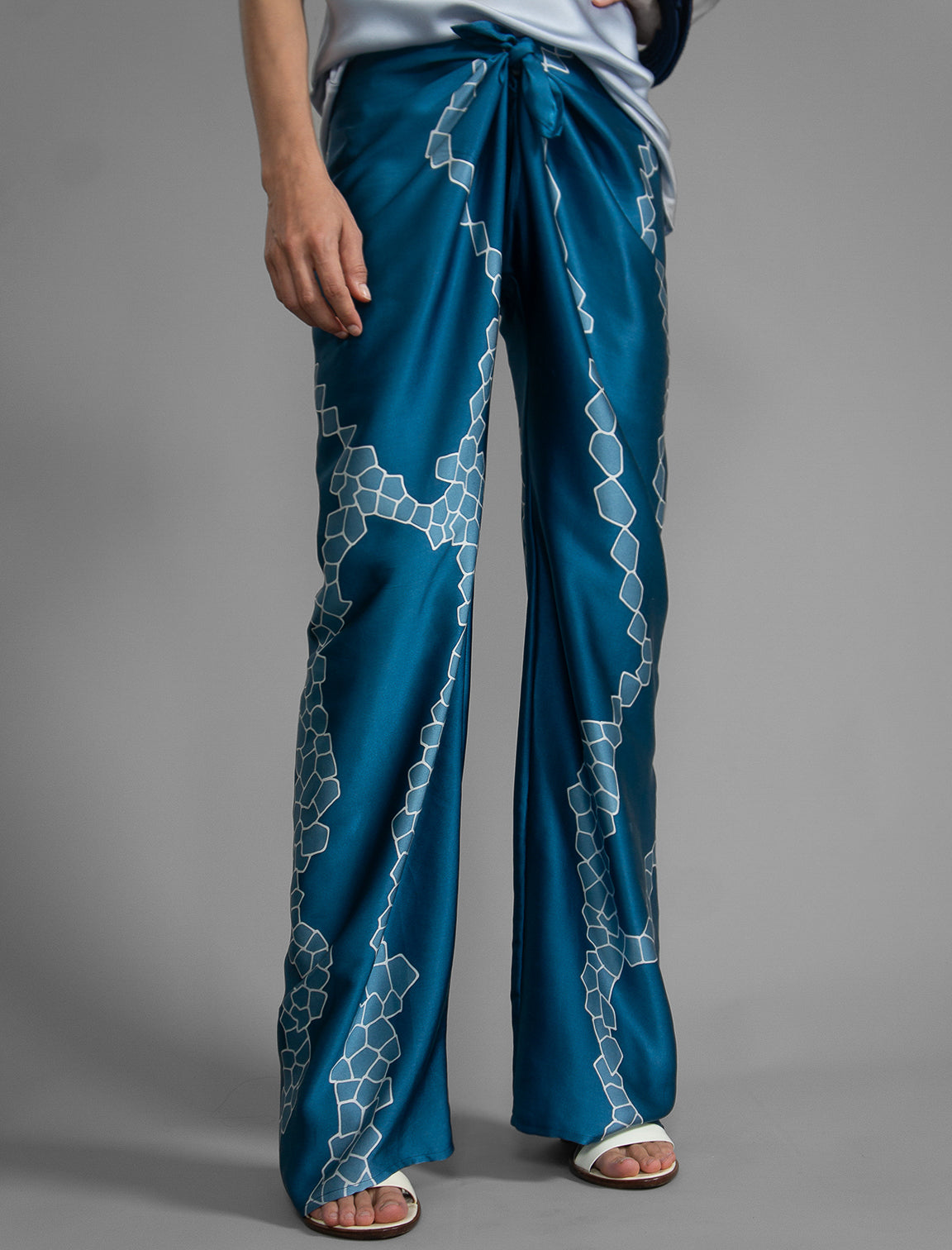 Close front view. Long silk pants in saxony blue colour with contrasting blue graphic Macrosnake batik motif, featuring a knot tie at the front and a slick relaxed silhouette. 