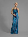 Front view. Elegant long body contouring silk dress in saxony blue colour with contrasting blue graphic Macrosnake batik motif, featuring spaghetti straps, V-neckline and a fluid contemporary silhouette.