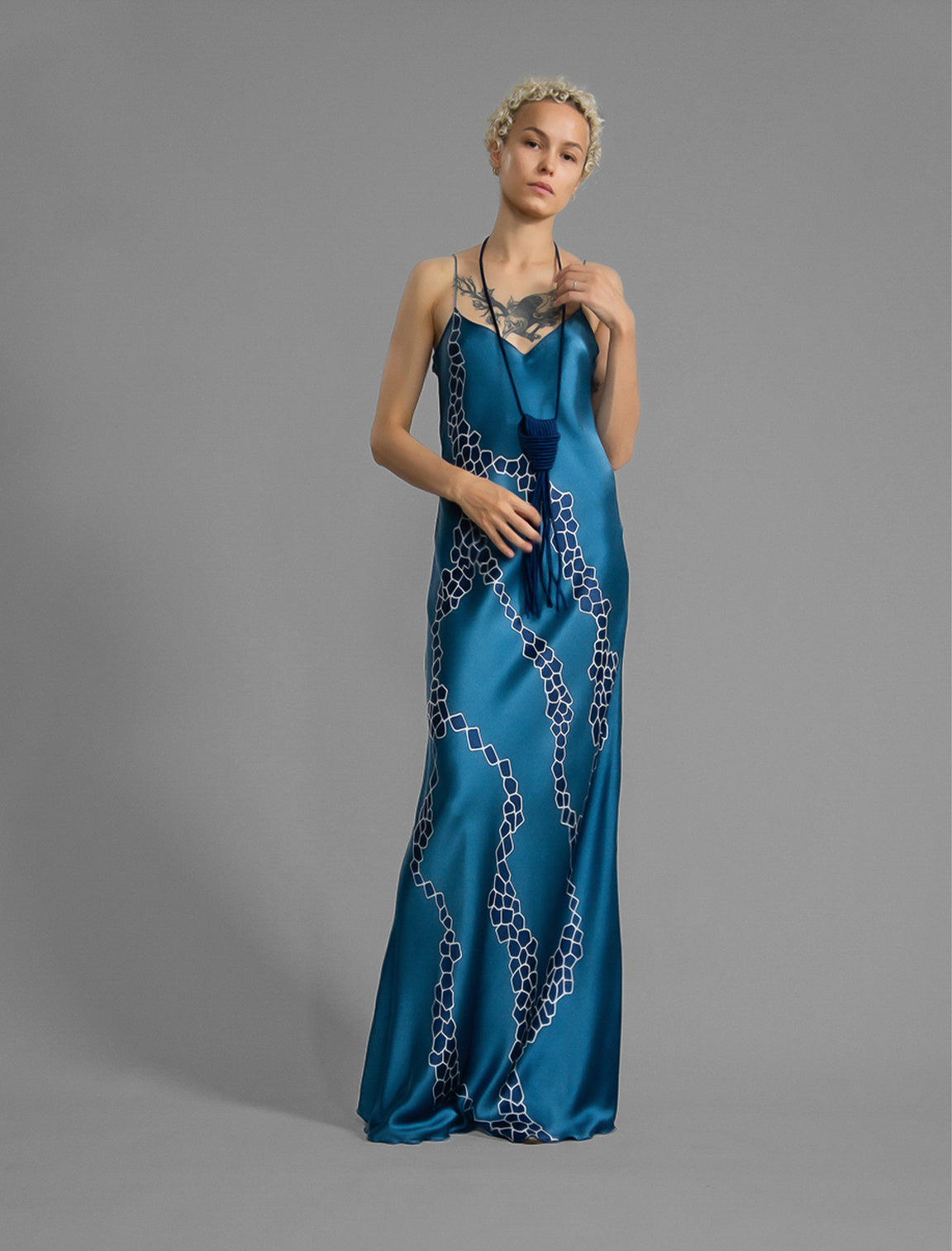 Front view. Elegant long body contouring silk dress in saxony blue colour with contrasting blue graphic Macrosnake batik motif, featuring spaghetti straps, V-neckline and a fluid contemporary silhouette.