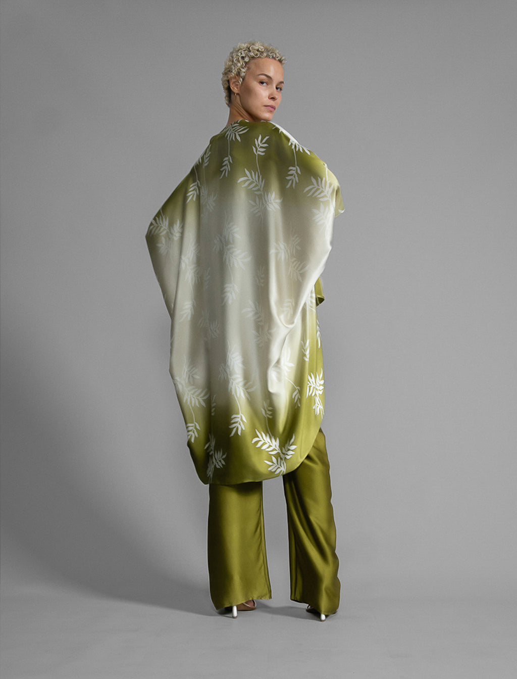 Back view. Relaxed flowing silk kaftan with subtle Dedaun leaf motif in moss green and white colour, featuring 3/4 length sleeves and a voluminous silhouette.