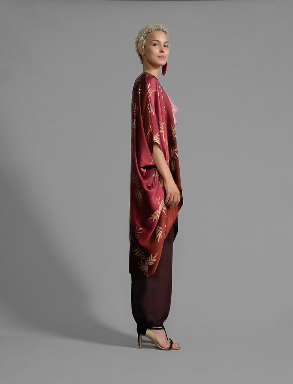 Right side view. Relaxed flowing silk kaftan with subtle Dedaun leaf motif in russet and raspberry colour, featuring 3/4 length sleeves and a voluminous silhouette.