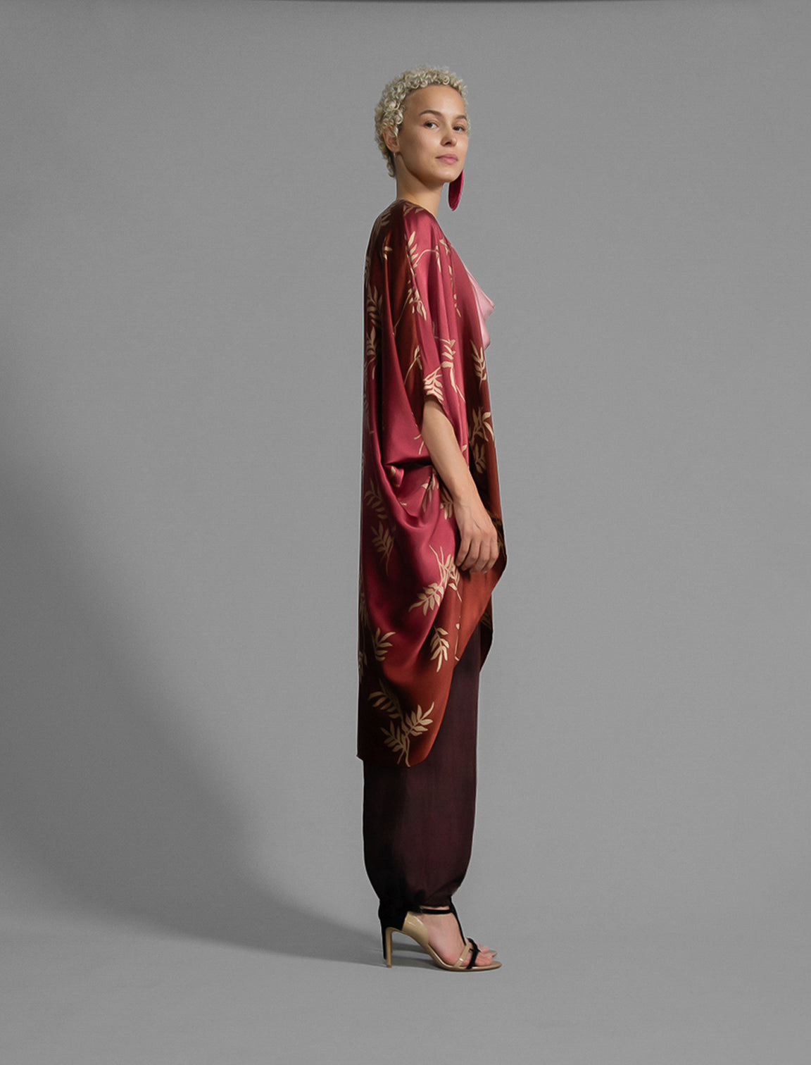 Right side view. Relaxed flowing silk kaftan with subtle Dedaun leaf motif in russet and raspberry colour, featuring 3/4 length sleeves and a voluminous silhouette.