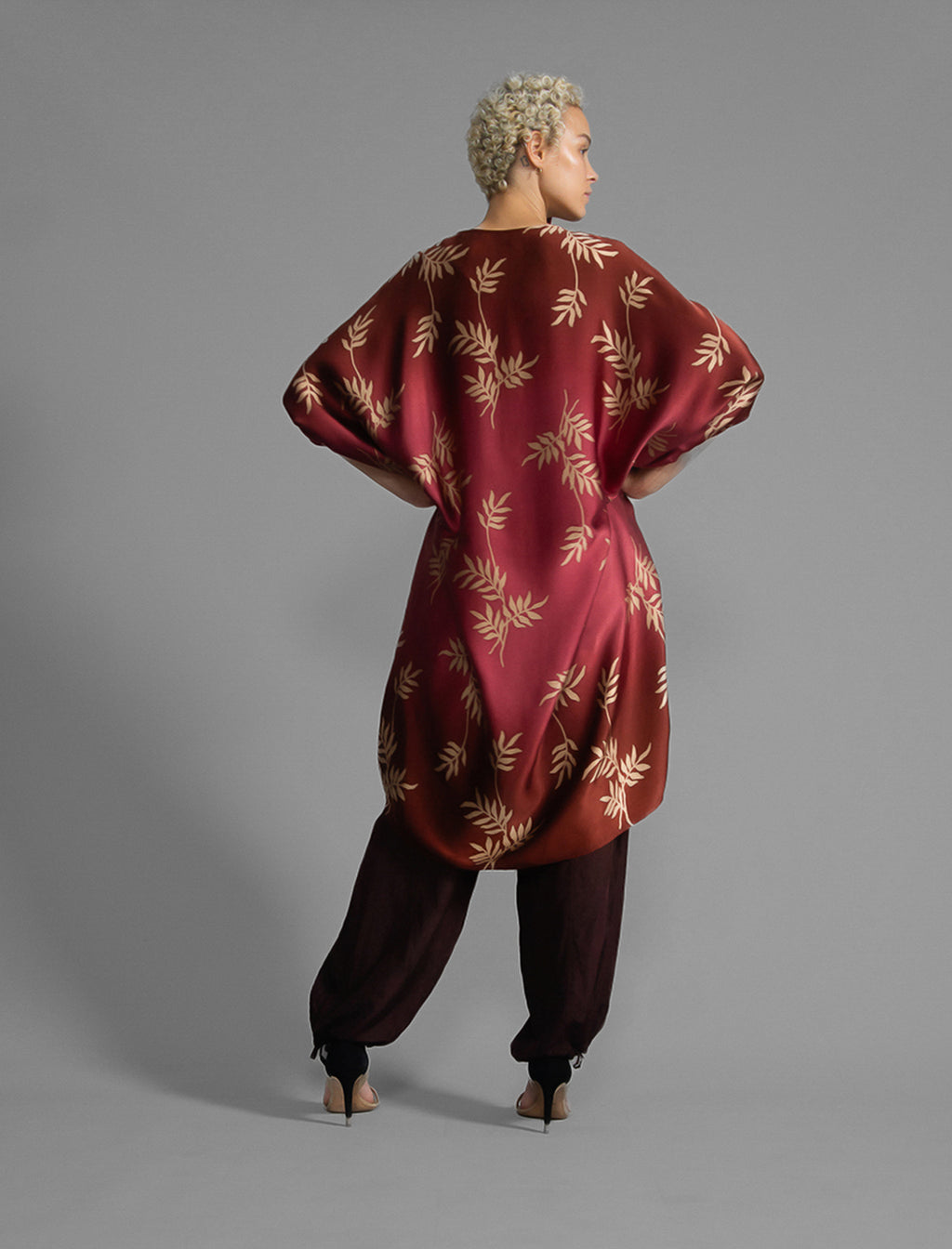 Back view. Relaxed flowing silk kaftan with subtle Dedaun leaf motif in russet and raspberry colour, featuring 3/4 length sleeves and a voluminous silhouette.