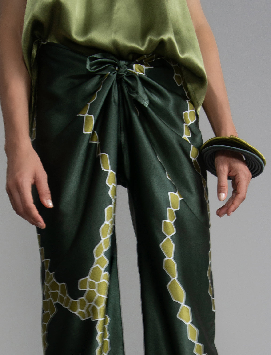 Knot detail: Long silk pants in forest green colour with contrasting green graphic Macrosnake batik motif, featuring a knot tie at the front and a slick relaxed silhouette. 