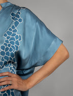 Left sleeve detail: Mid length shirt dress in dream blue colour with contrasting blue graphic Macrosnake batik motif, featuring short sleeves with deep hem, curved hemline, simple collar with narrow V-neckline and relaxed contemporary silhouette.