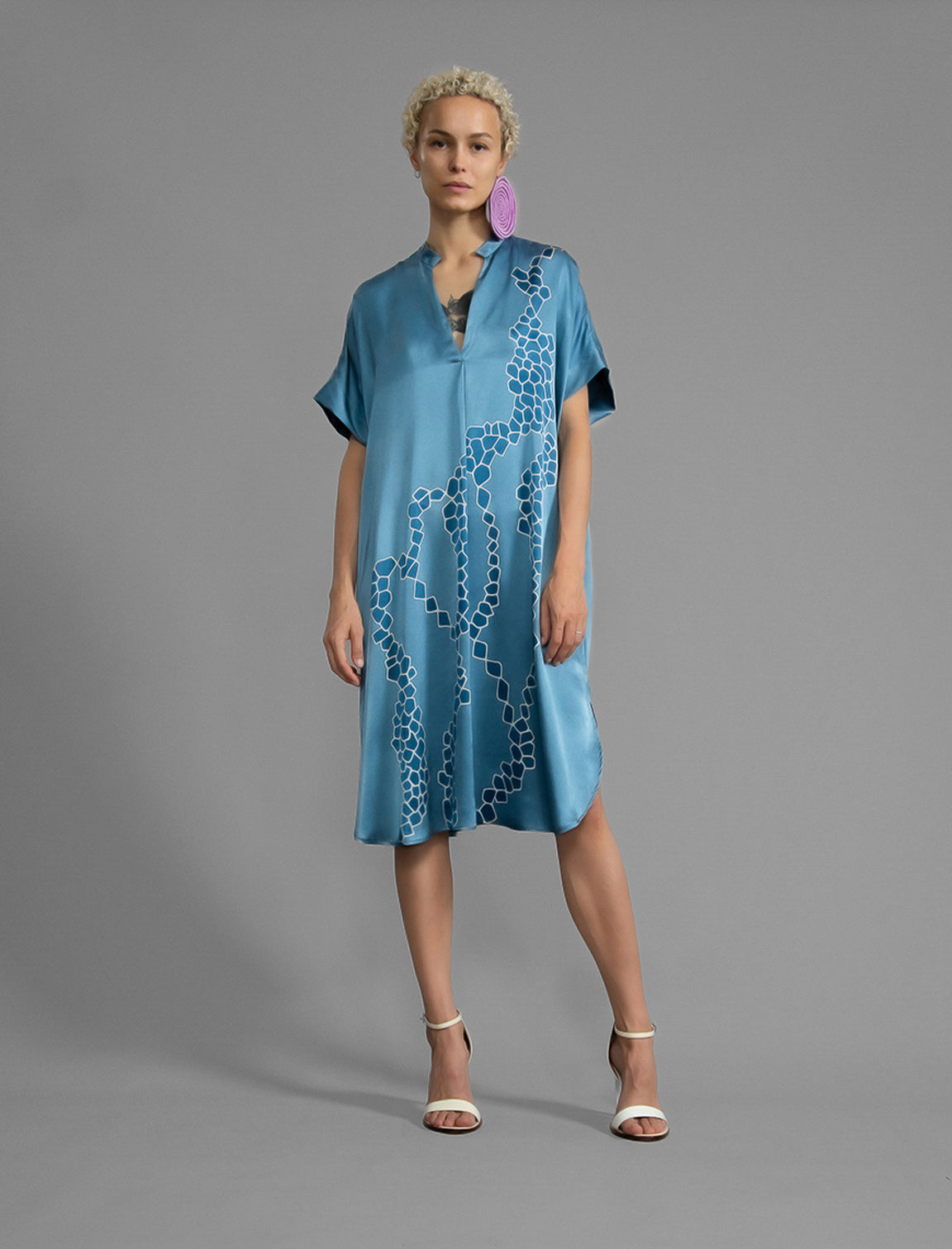 Front view. Mid length shirt dress in dream blue colour with contrasting blue graphic Macrosnake batik motif, featuring short sleeves with deep hem, curved hemline, simple collar with narrow V-neckline and relaxed contemporary silhouette.