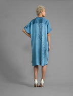 Back view. Mid length shirt dress in dream blue colour with contrasting blue graphic Macrosnake batik motif, featuring short sleeves with deep hem, curved hemline, simple collar with narrow V-neckline and relaxed contemporary silhouette.