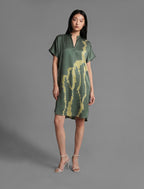 Front view. Mid length shirt dress in forest green colour with contrasting lime graphic Macrosnake batik motif, featuring short sleeves with deep hem, curved hemline, simple collar with narrow V-neckline and relaxed contemporary silhouette.