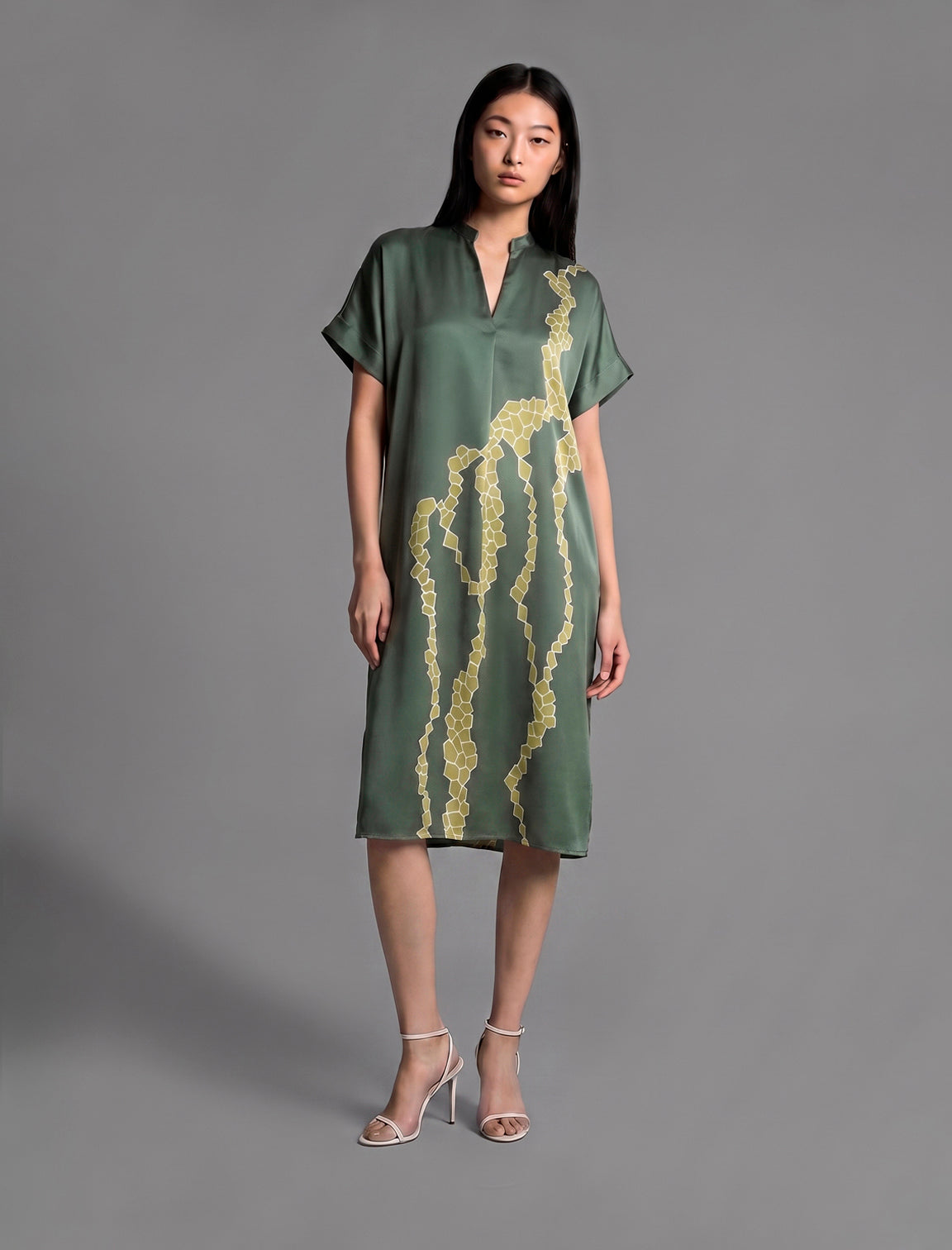 Front view. Mid length shirt dress in forest green colour with contrasting lime graphic Macrosnake batik motif, featuring short sleeves with deep hem, curved hemline, simple collar with narrow V-neckline and relaxed contemporary silhouette.