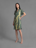Side view. Mid length shirt dress in forest green colour with contrasting lime graphic Macrosnake batik motif, featuring short sleeves with deep hem, curved hemline, simple collar with narrow V-neckline and relaxed contemporary silhouette.