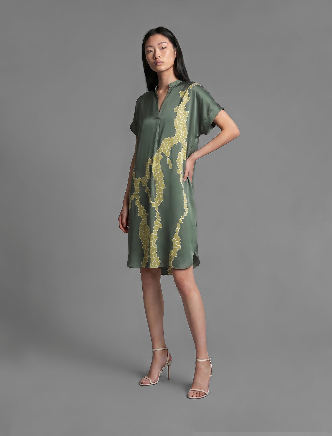 Side view. Mid length shirt dress in forest green colour with contrasting lime graphic Macrosnake batik motif, featuring short sleeves with deep hem, curved hemline, simple collar with narrow V-neckline and relaxed contemporary silhouette.
