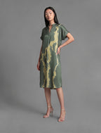 Left side view. Mid length shirt dress in forest green colour with contrasting lime graphic Macrosnake batik motif, featuring short sleeves with deep hem, curved hemline, simple collar with narrow V-neckline and relaxed contemporary silhouette.