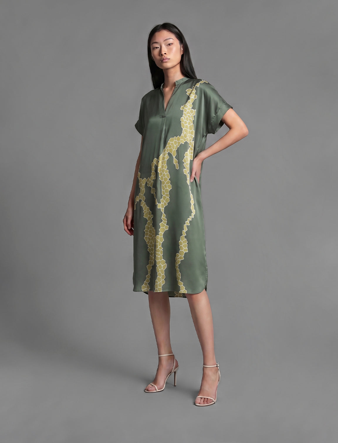 Left side view. Mid length shirt dress in forest green colour with contrasting lime graphic Macrosnake batik motif, featuring short sleeves with deep hem, curved hemline, simple collar with narrow V-neckline and relaxed contemporary silhouette.