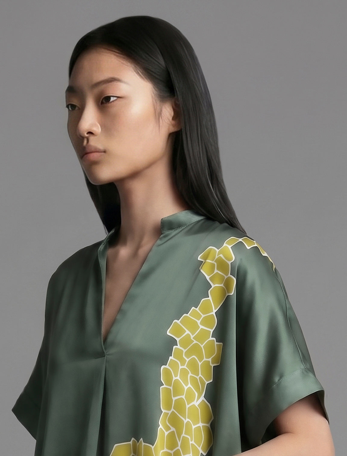 Neckline detail view. Mid length shirt dress in forest green colour with contrasting lime graphic Macrosnake batik motif, featuring short sleeves with deep hem, curved hemline, simple collar with narrow V-neckline and relaxed contemporary silhouette.