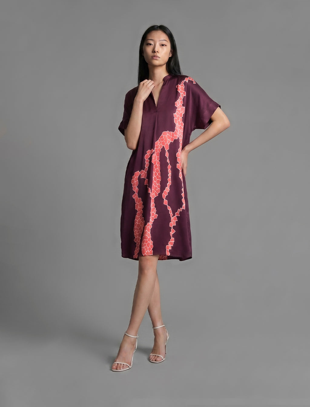 Front view. Mid length shirt dress in deep vino colour with contrasting bright pink graphic Macrosnake batik motif, featuring short sleeves with deep hem, curved hemline, simple collar with narrow V-neckline and relaxed contemporary silhouette.