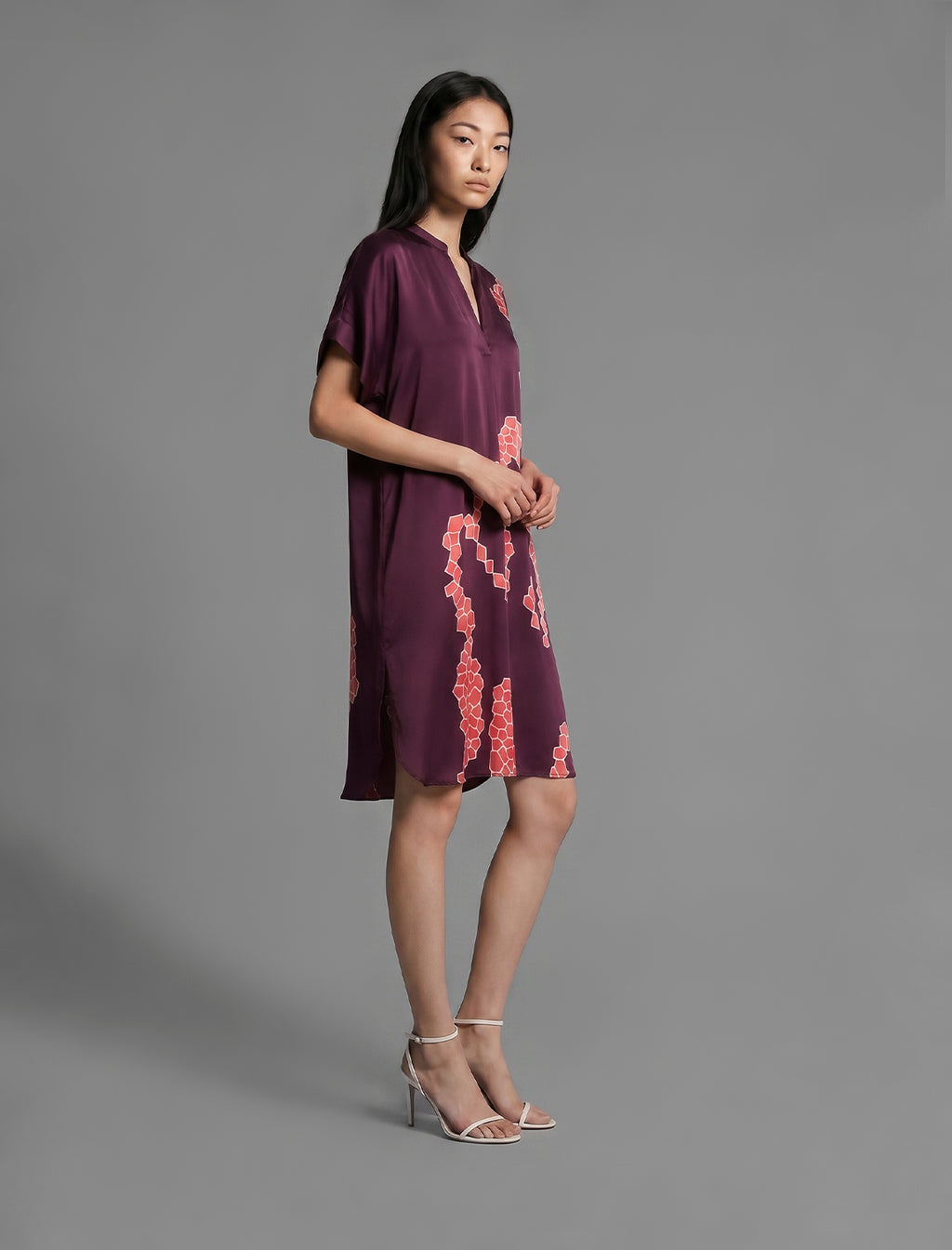 Side view. Mid length shirt dress in deep vino colour with contrasting bright pink graphic Macrosnake batik motif, featuring short sleeves with deep hem, curved hemline, simple collar with narrow V-neckline and relaxed contemporary silhouette.
